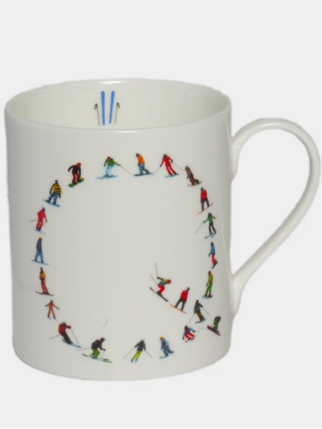 A simple white mug illustrated with a ‘Q’ made of small, multicoloured skiers. The mug is set against a plain, white background.
