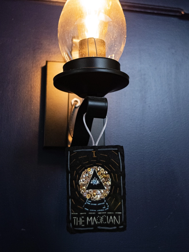 A handcrafted felt ornament with sequins and embroidery depicting "The Magician" tarot card. Colourful embroidery with an eye inside a crystal ball. 