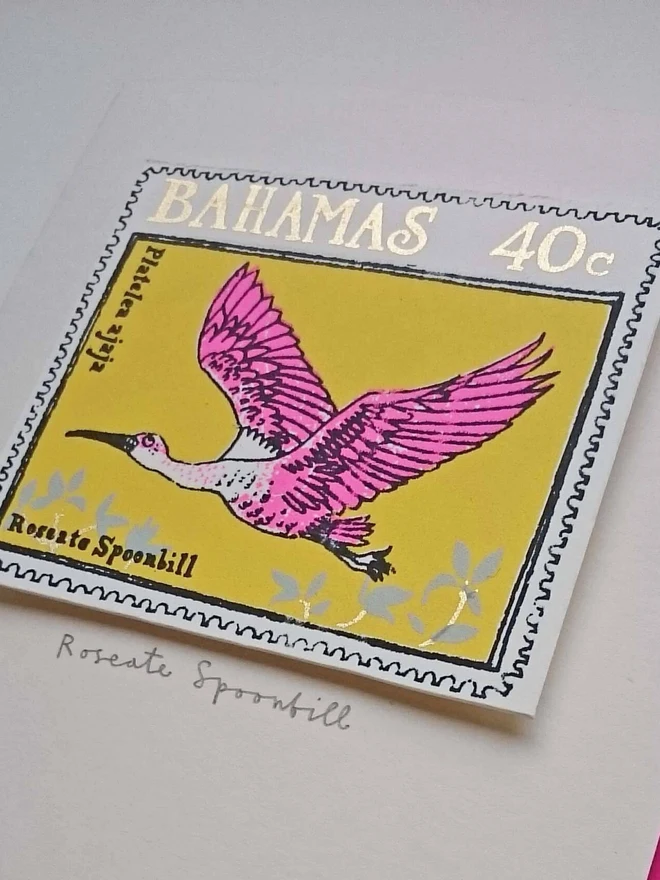 Bird Stamp Card Roseate Spoonbill/ Bahamas, a white card with a colourful bird design in the centre on top of a white surface. 