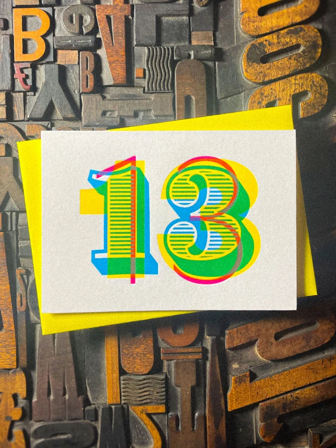 Luxury handmade 13th birthday letterpress card paired with a vibrant yellow envelope. The oversized number 13 is printed in overlapping cyan, magenta and yellow inks, creating additional green, orange and deeper colours where the inks meet.
