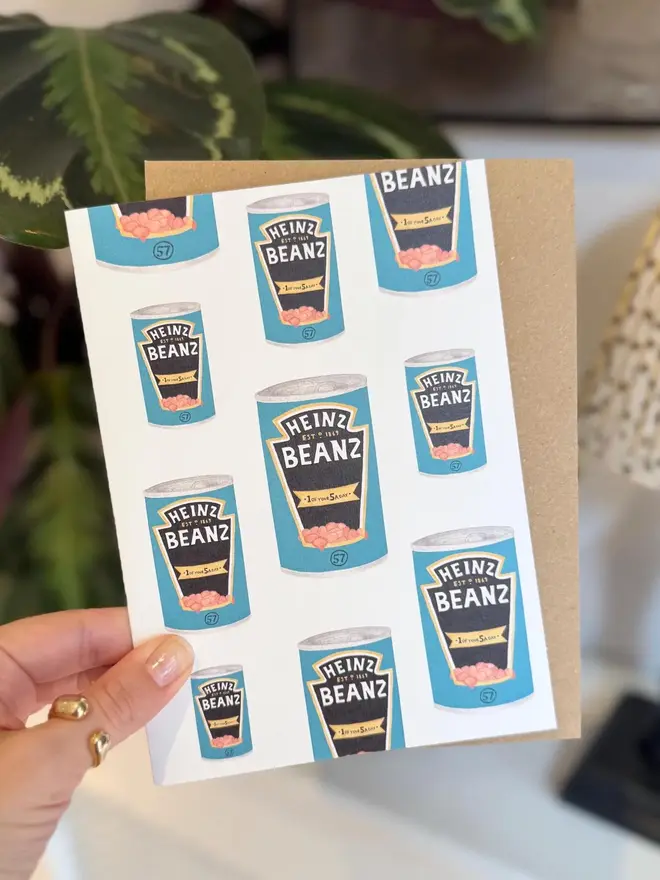 baked beans tins illustrated card. card photographed with brown kraft envelope with houseplants in background.