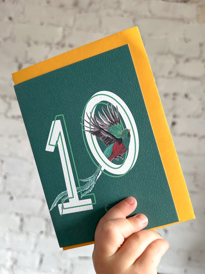 Deep green card featuring a big white number 10 and an illustration of a quetzal bird alongside a yellow envelope