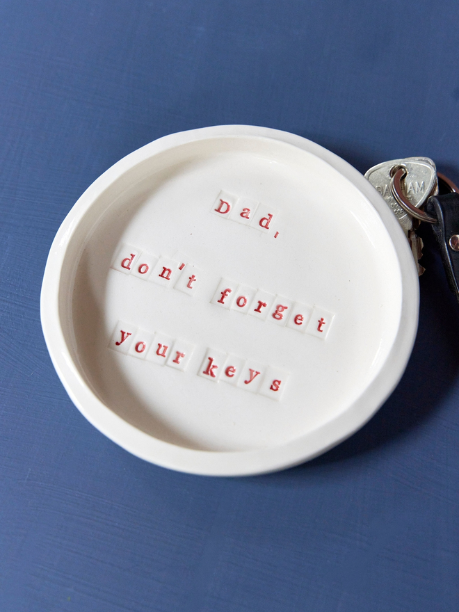 Ceramic small plate with the phrase 'Dad, don't forget your keys' stamped on the front in red lettering