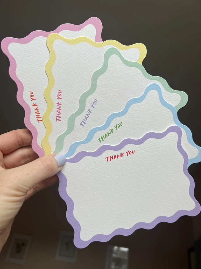 Five wavy edged notecards with different coloured borders and the words Thank You written in capital letters