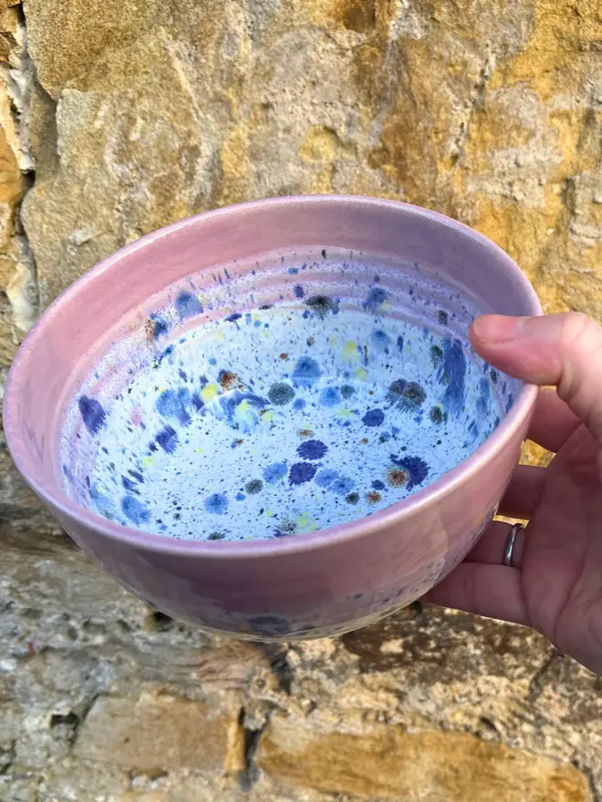 Shoreline Small Bowl, a colourful bowl held in front of a brick wall. 