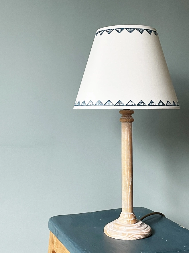 Hand-painted linen empire lampshade with a navy blue geometric triangle border, shown on a natural wooden table lamp. This neutral lampshade features a clean white body with a bold patterned edge, creating elegant geometric lighting and a timeless, handcrafted look suitable for table lamps.