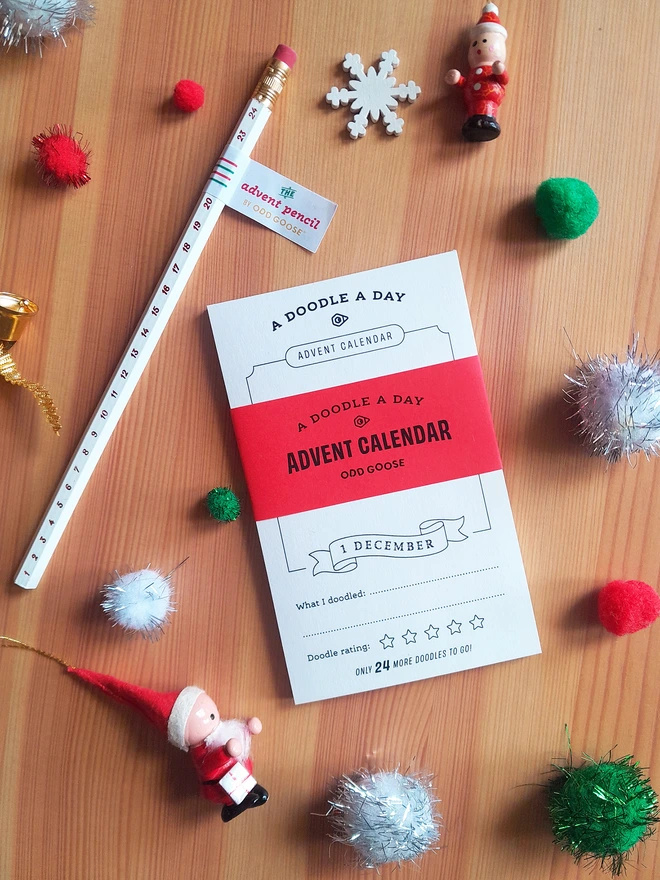 Odd Goose Creative Stationery Advent Calendar notepad and foil printed pencil seen top down with Christmas decorations