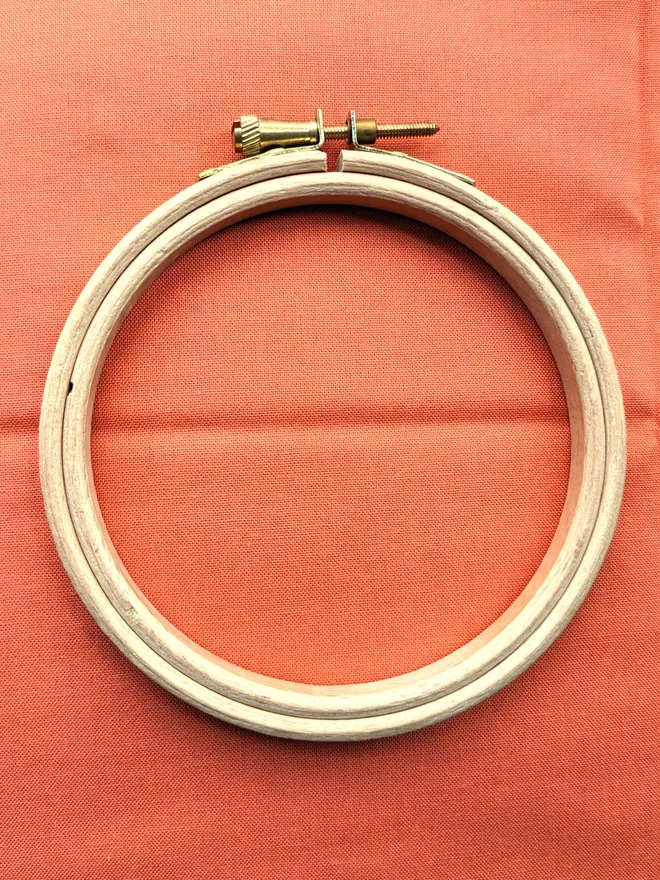 A wooden embroidery hoop lying on a piece of coral coloured fabric