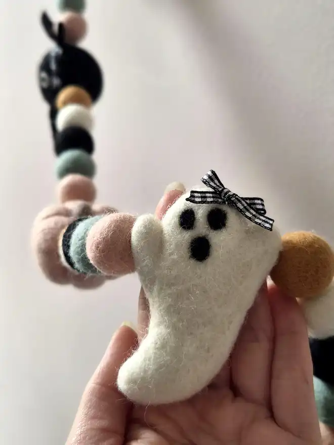 A hand holding a felt ghost with a gingham bow.
