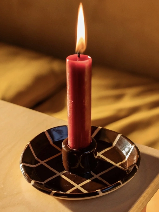Ceramic Patterned Candlestick Holder, a colourful candlestick holder sitting on a table stop surface. It is accompanied by a lit candle. 