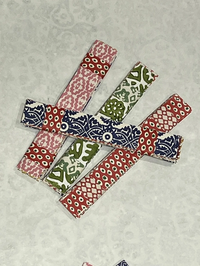 Colourful Paperchains (Set Of 60). Bundles of folded patterned paper strips in pink, green, navy and red, each held together with a contrasting paper band. These ready-cut strips are the pieces used to make a decorative paper chain garland.