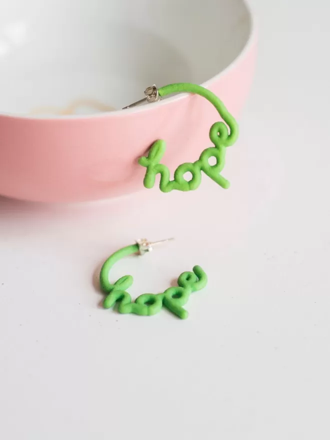 Small Hope Hoop earrings in green small seen in a pink bowl.