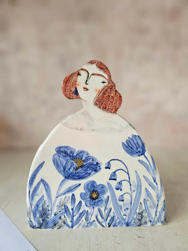 a large vase shaped like a lady with red hair looking up with blue flowers painted on her dress, front view