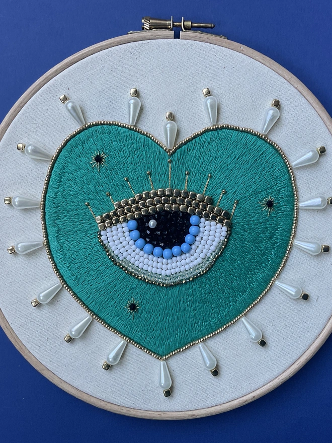 An embroidery hoop containing a hand stitched with a beaded protective eye within it