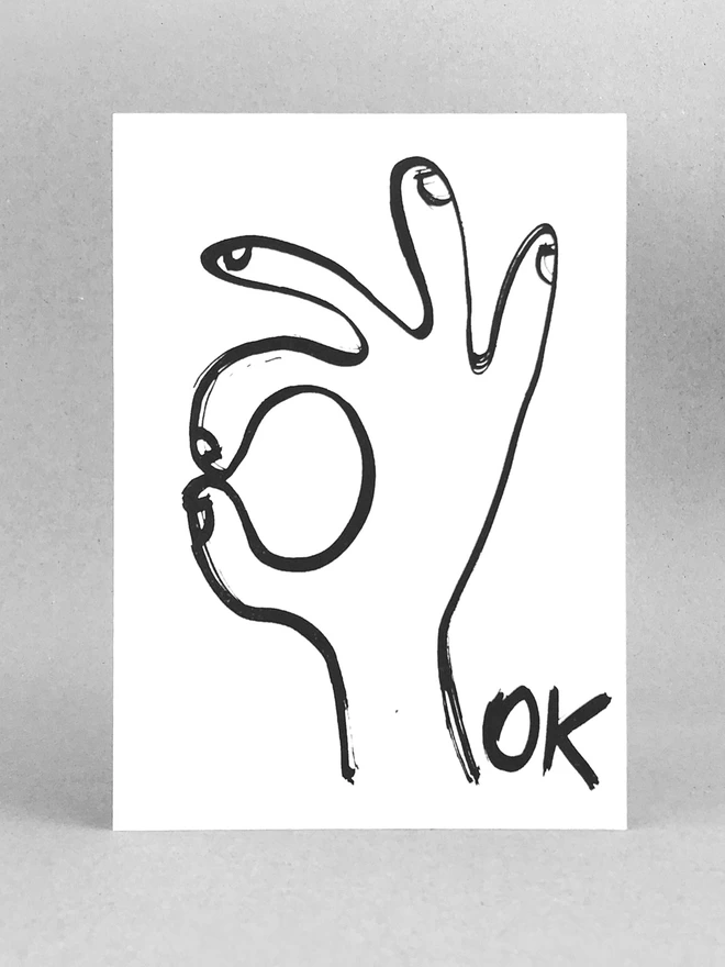 A white Ok Greetings Card with a black ink drawn hand and the word ok, front on view made by Salty's Studio.