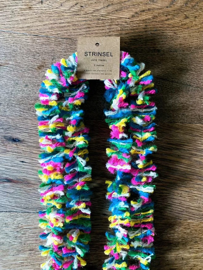 2 metre length of multicolour neon Strinsel (plastic free string tinsel) with label on oak table