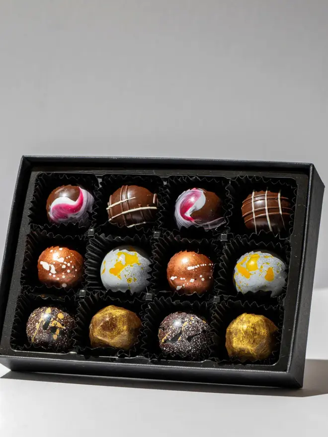 The original gallery chocolates in a black box on a white table, pack of 12. 
