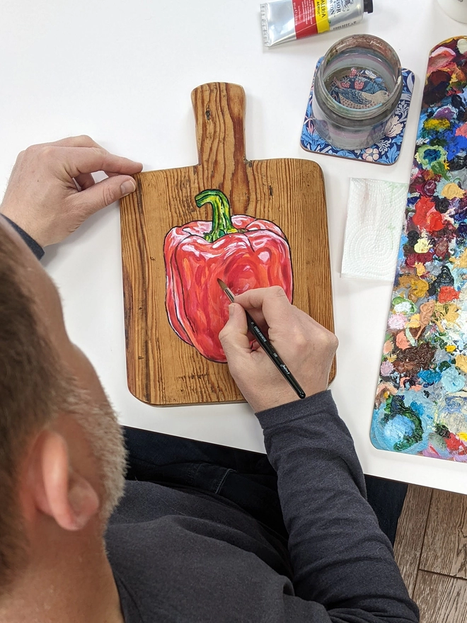 Artist creating a wooden chopping board with handpainted design of a red pepper