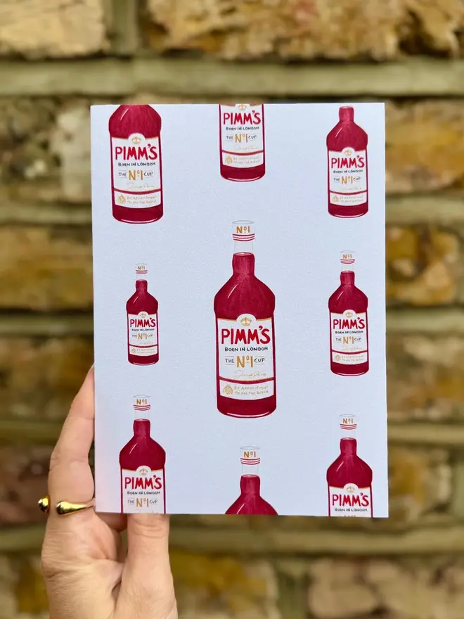 pimms bottle illustrated card. card photographed against brick wall backdrop.