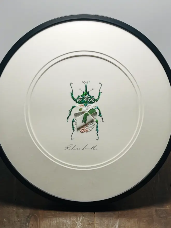 Hand-drawn, painted, mosaic clay, vintage green Chinese Dragon pottery insect on white double mounted card, in a black circular frame.
