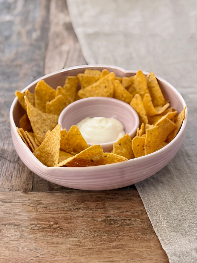 Heart shaped chip and dip bowl with tortilla chips and dip on a rustic wooden table