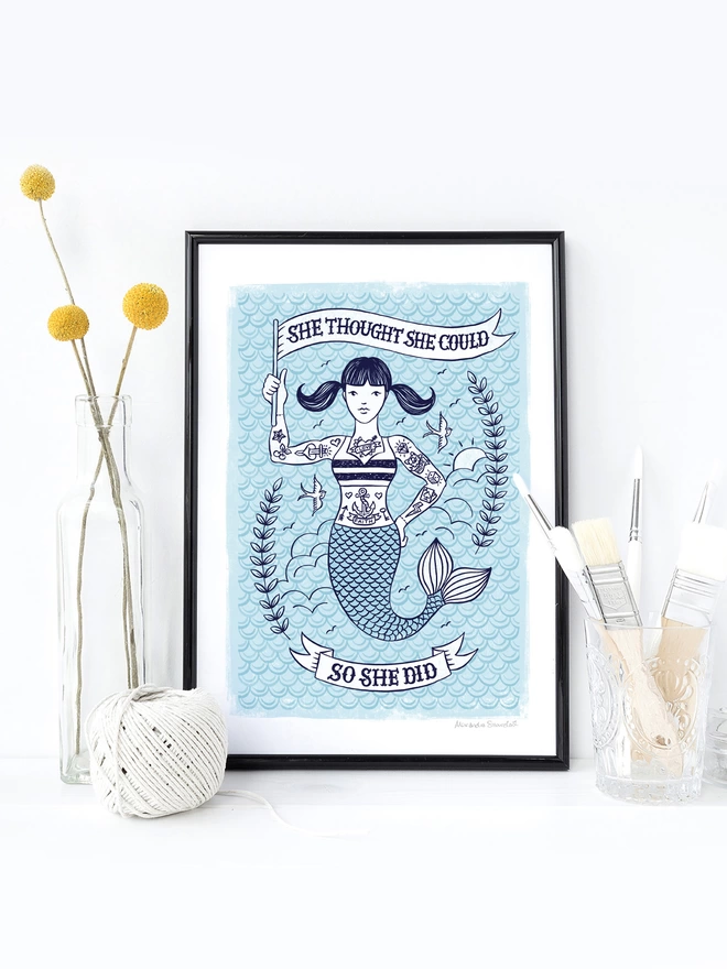 blue and white tattooed mermaid print in black frame with yellow flowers and white make up brushes