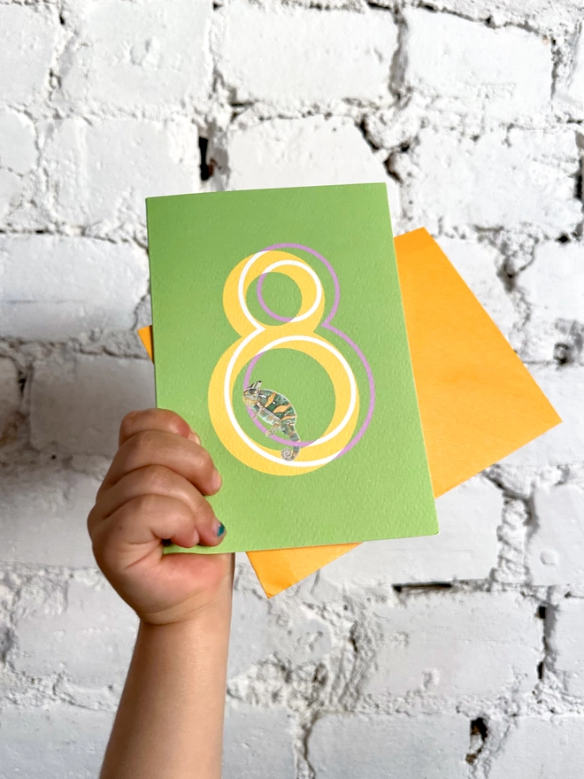 a bright green card with a big yellow number 8 and an illustrated chameleon with a bright yellow envelope