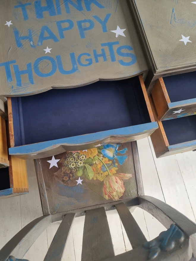 Vintage painted dressing table and chair. Painted in coffee grey and decorated using layered antique florals with yellow and blue accents and finished with hand-cut white paper stars. Text reads in blue 'think happy thoughts'. Heavily distressed finish.