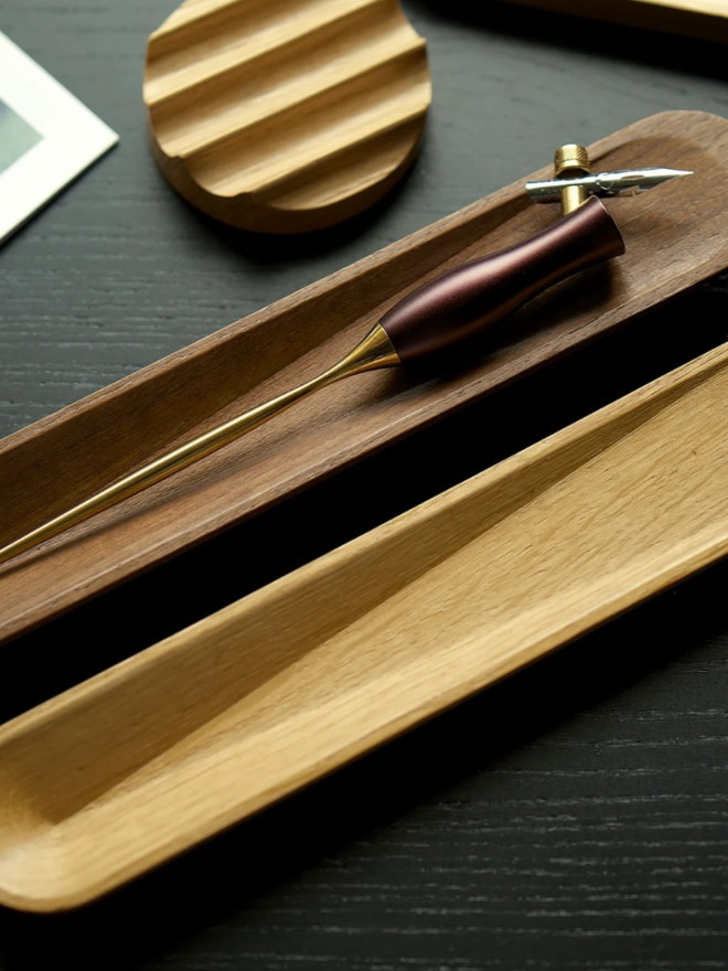 Pen Rest. Oak and Walnut pen rests sat together on a desk. The Walnut colour is significantly darker than the Oak.