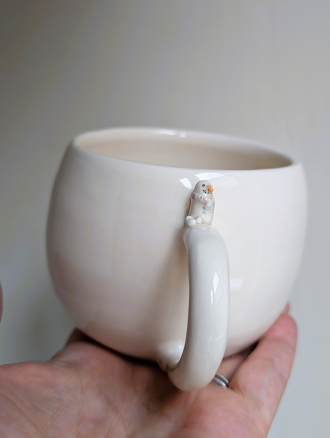 white cup with a tiny ceramic snowman and snowballs on the handle 