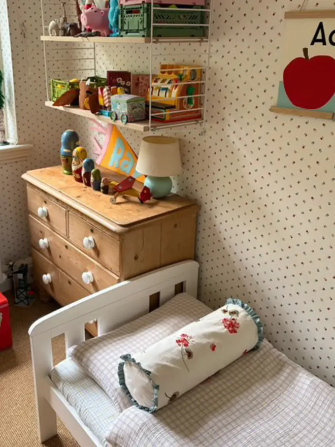 Embroidered floral bolster cushion with blue ruffle trim, styled on a child’s bed in a colourful patterned bedroom.