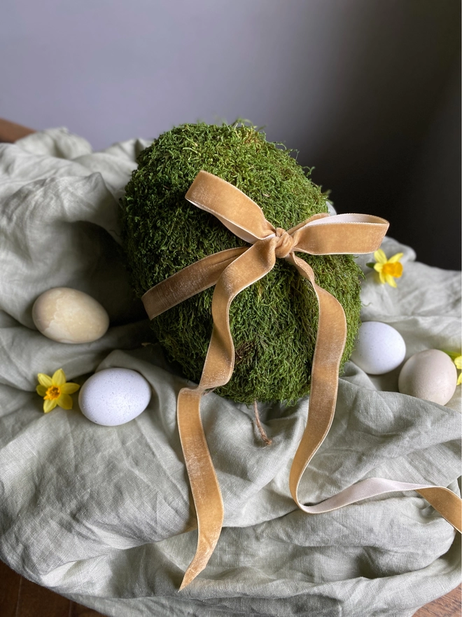 Mossed egg sitting on linen fabric with gold velvet bow
