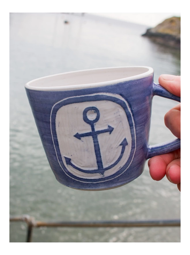 someone holding the anchor mug in front of the Cornish sea