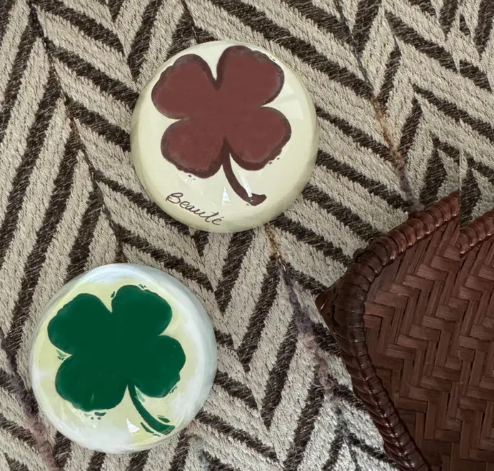 Two round clover paperweights on patterned fabric beside a woven basket.