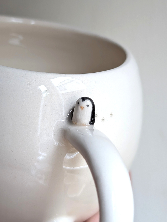 white cup with a tiny ceramic penguin on the handle 