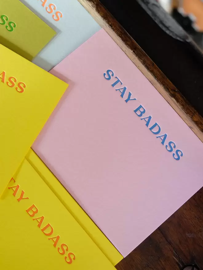 Candy pink notecard with 'Stay Badass' letterpress printed in bright blue ink. 