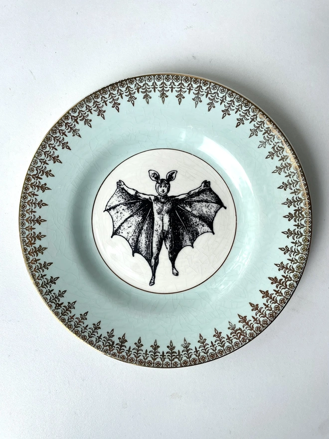 vintage plate with an ornate border, with a printed vintage illustration of a bat boy in the middle 