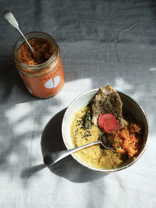 Ferment Intro Journey (Set Of 5), a jar of ferment sitting on a dining table. It is accompanied by other foods and drinks on a white surface. 