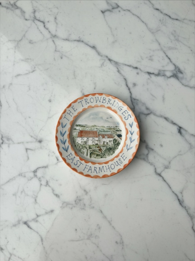 Multicoloured house plate, country house inset with name of house and botanical border around, edged in cheery orange.