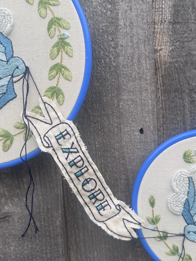 A close up of an embroidered banner with the words find explore stitched onto it