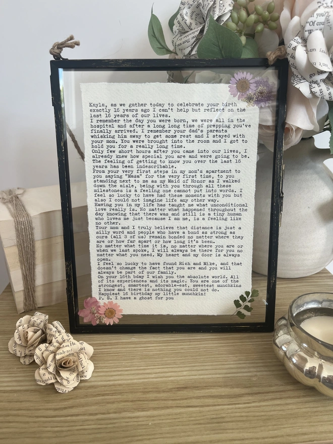 Framed typewriter print hand typed with an antique typewriter onto cotton rag handmade deckled paper. It is displayed in a black hanging rustic frame with gold brush detailing and decorated with real pressed dried flowers.