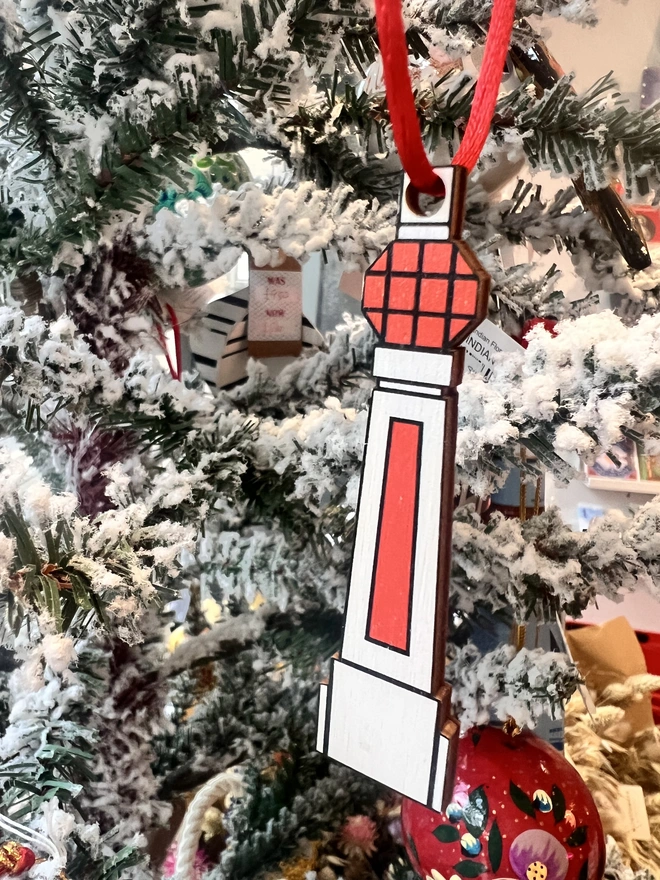 Small white and orange wooden tree decoration in the shape of Margate Lido sign. It is hanging by a red thread on a white fake Christmas Tree with other decorations.