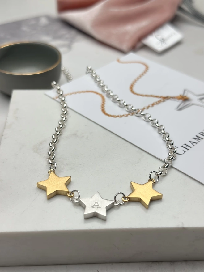 3 chunky star charms hang horizontally from a sterling silver chain.  a personalised silver star hangs in the middle with gold stars on each side