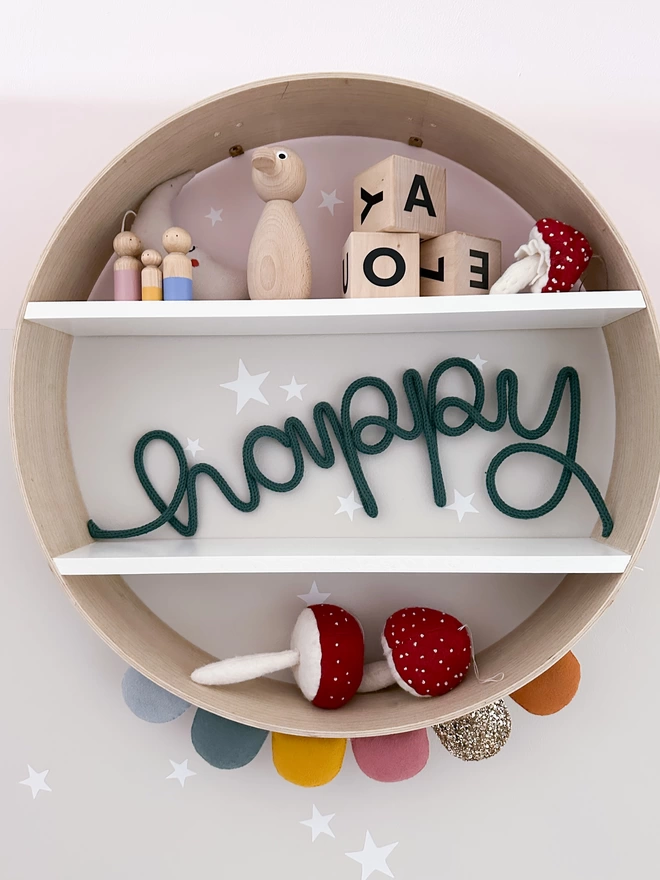 'happy' knitted wooly wire word wall decor on a circular shelf decorated with Scandinavian style modern props and a scallop felt garland with star stickers on the wall. 