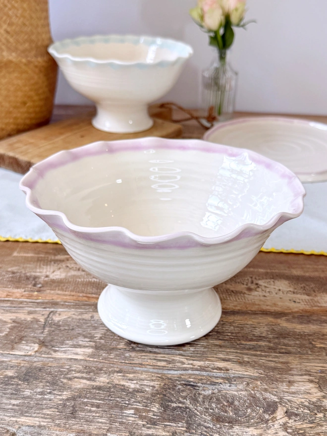 Undulating hand thrown porcelain stem bowls with satin cream glaze and pink or turquoise rim on a rustic table top
