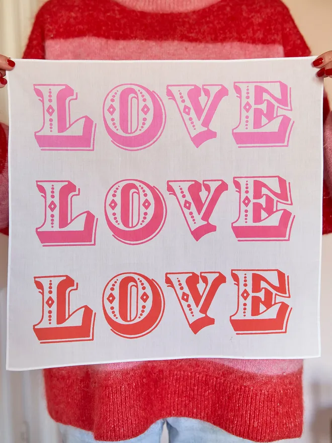 LOVE LOVE LOVE printed cotton handkerchief being held up against a red and pink striped jumper