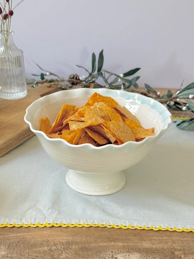 undulating rim hand thrown stem bowl with turquoise blue edge on rustic table with crisps