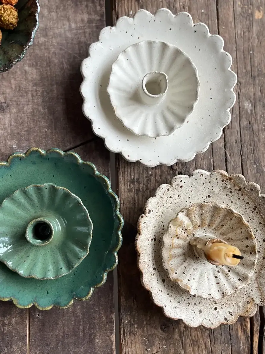Handmade Scalloped Ceramic Dish, a collection of colourful ceramic plates on a wooden surface. They are accompanied by some candlestick holders. 
