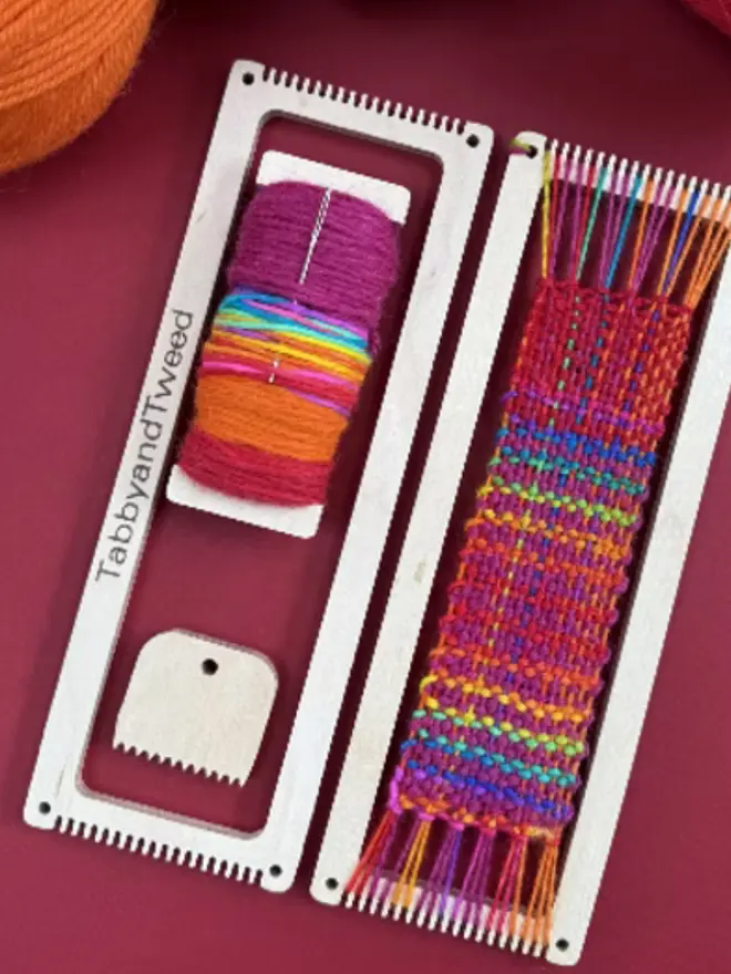 Rectangular beige looms, one woven with bright rainbow coloured yarns with a spool of bright yarn and wooden comb.