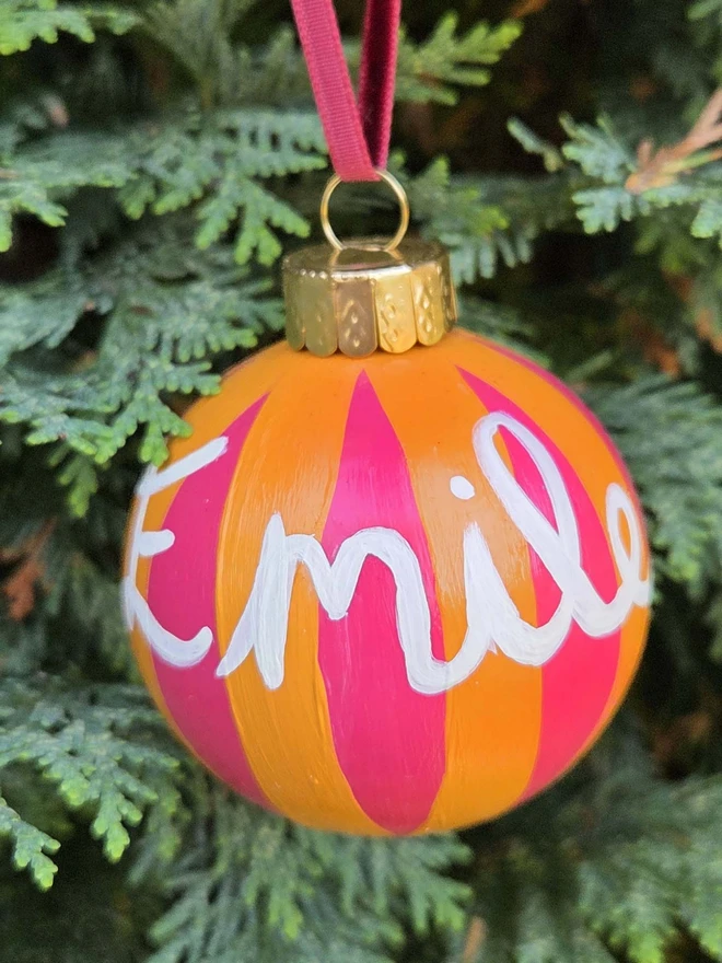 hand painted yellow and pink stripe bauble with name personalisation, hanging on a christmas tree